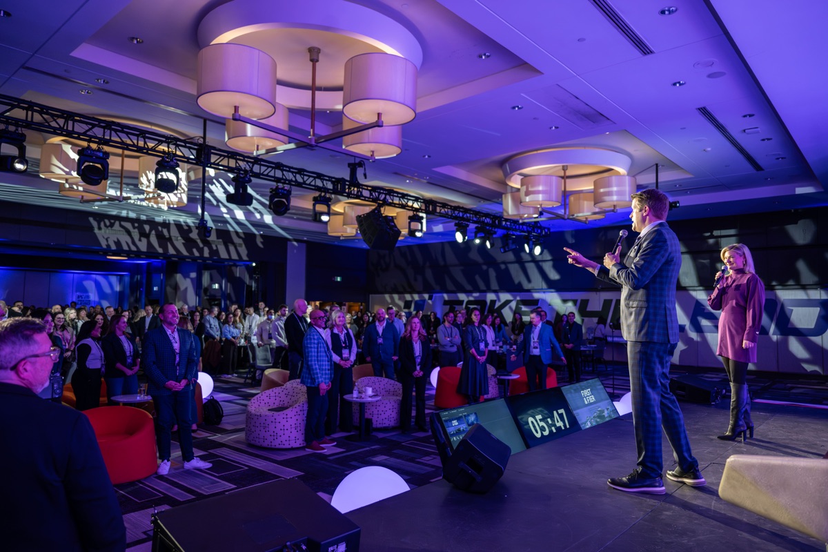 Speakers addressing a standing crowd at corporate event