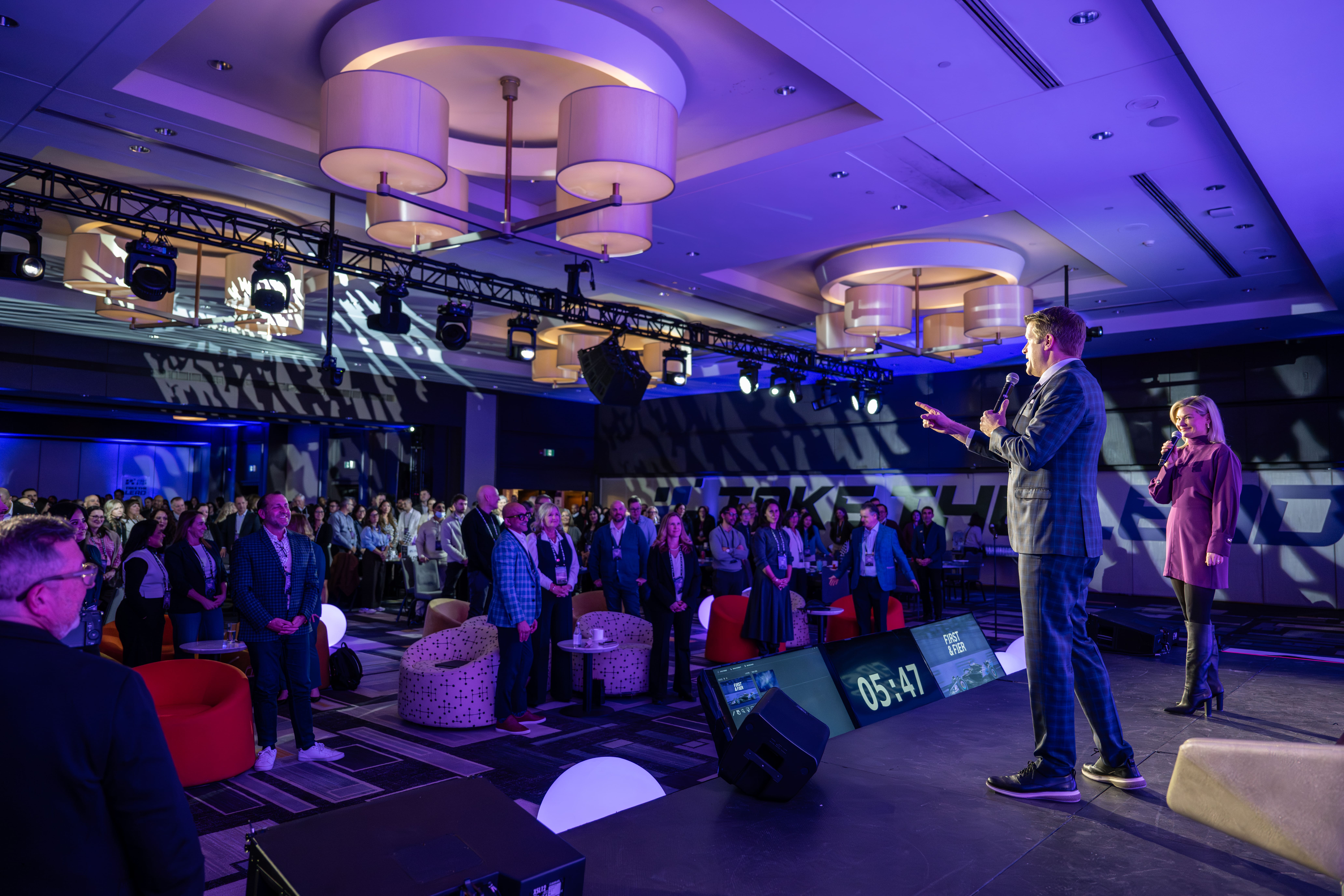 Speakers addressing a standing crowd at corporate event